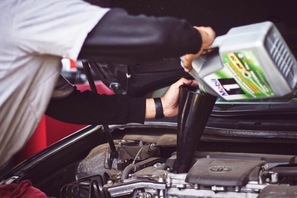 a man with a black watch filling a car engine with oil