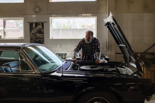 An older man in a checkered shirt examining the engine of a black car