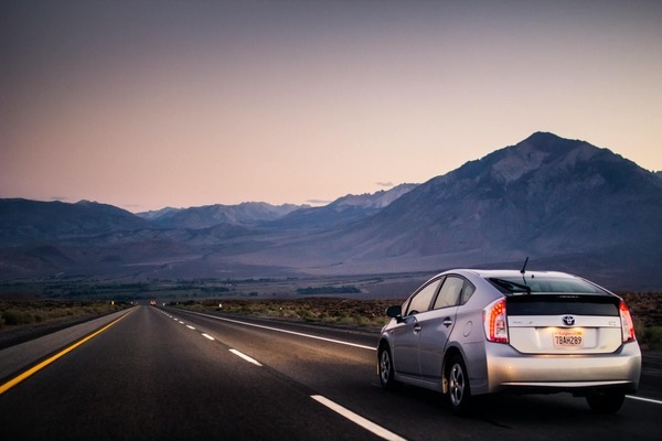 Silver Toyota Prius Hatchback driving down a desert road toward mountains